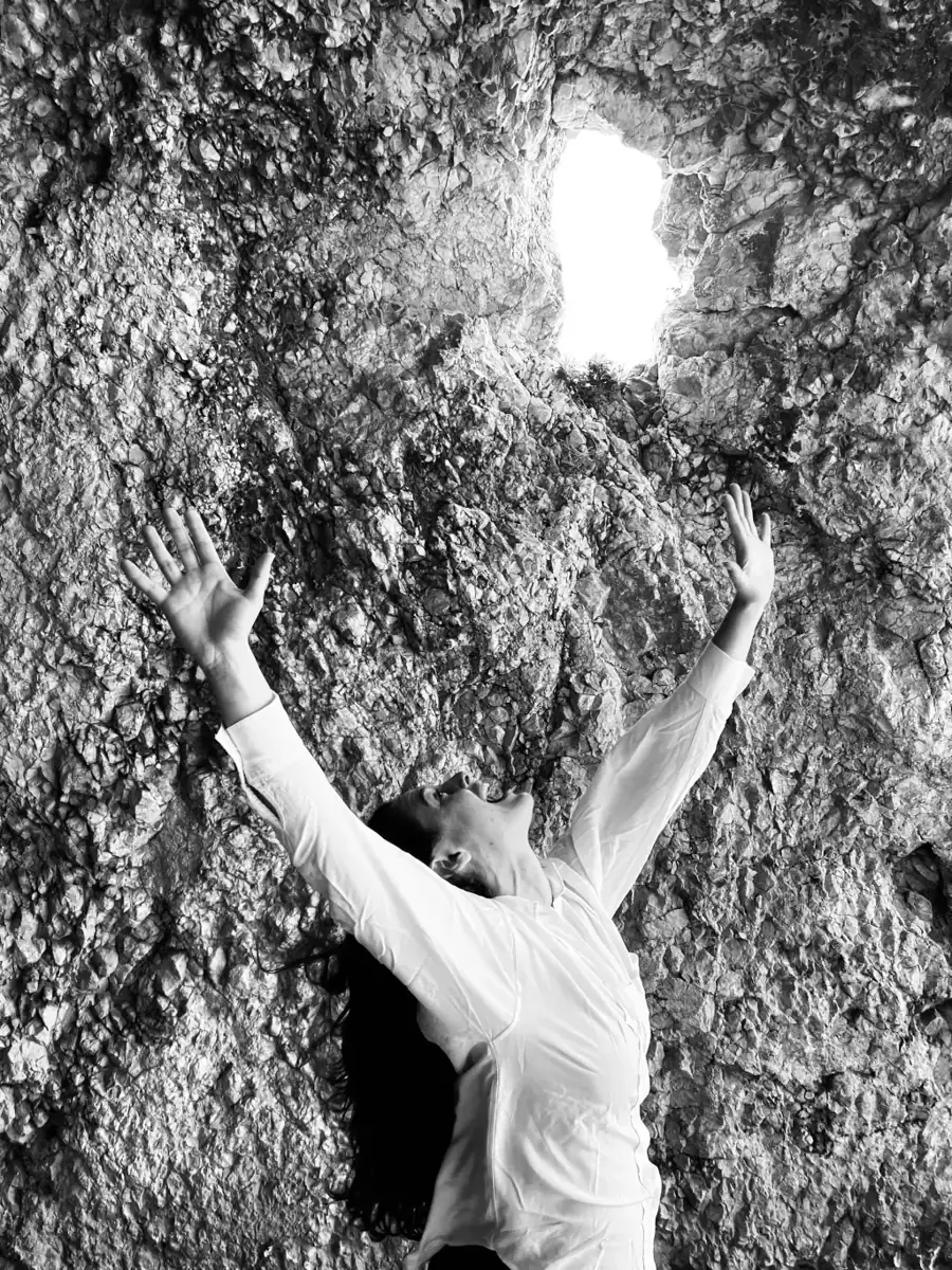 Alba Berrocal con los brazos extendidos hacia un haz de luz entre las rocas, fotografía en blanco y negro