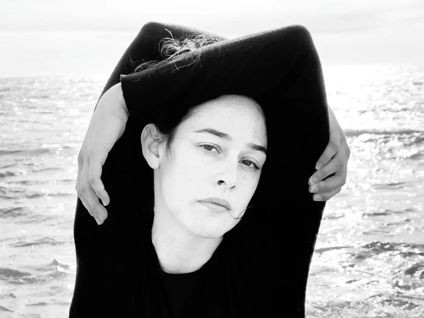 Retrato de Alba Berrocal junto al mar, con los brazos alrededor de la cabeza.